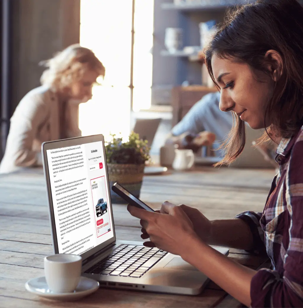 Woman looking into her phone with her laptop showing a webpage with display ads