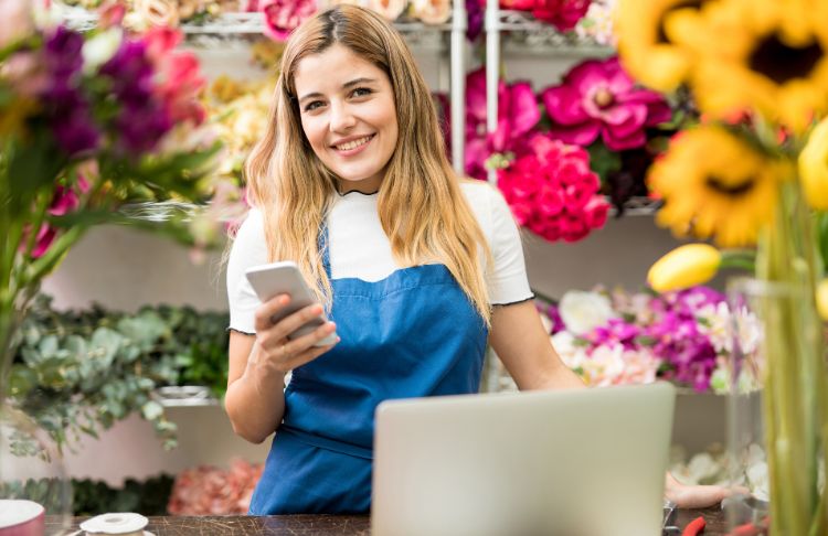 female business owner checking social media on phone in front of laptop