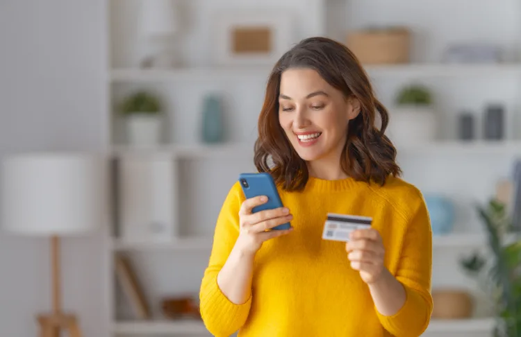 How to influence buyers - Woman looks at phone with credit card in her hand.